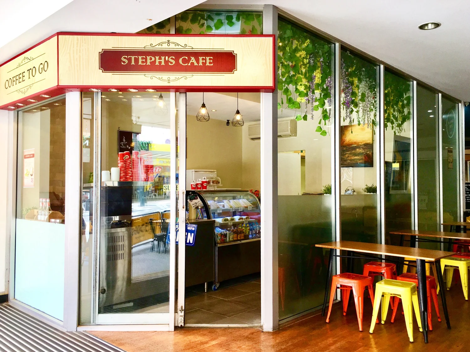 Steph’s Cafe’s red and yellow sign, coffee window and colourful stools at McWhirters